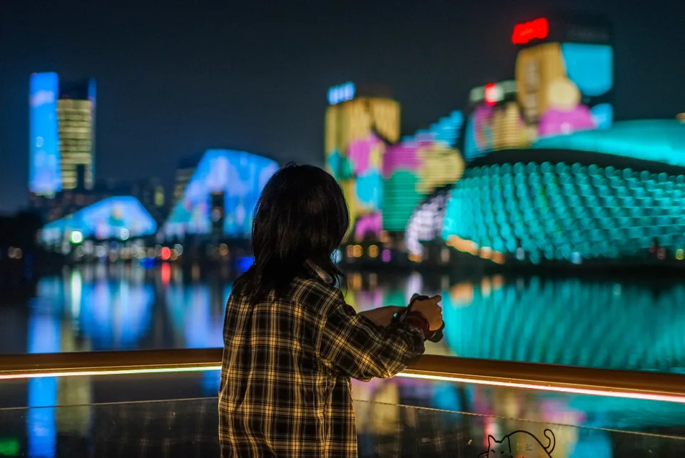 夜晚倚在水边栏杆旁的人与彩色城市灯光