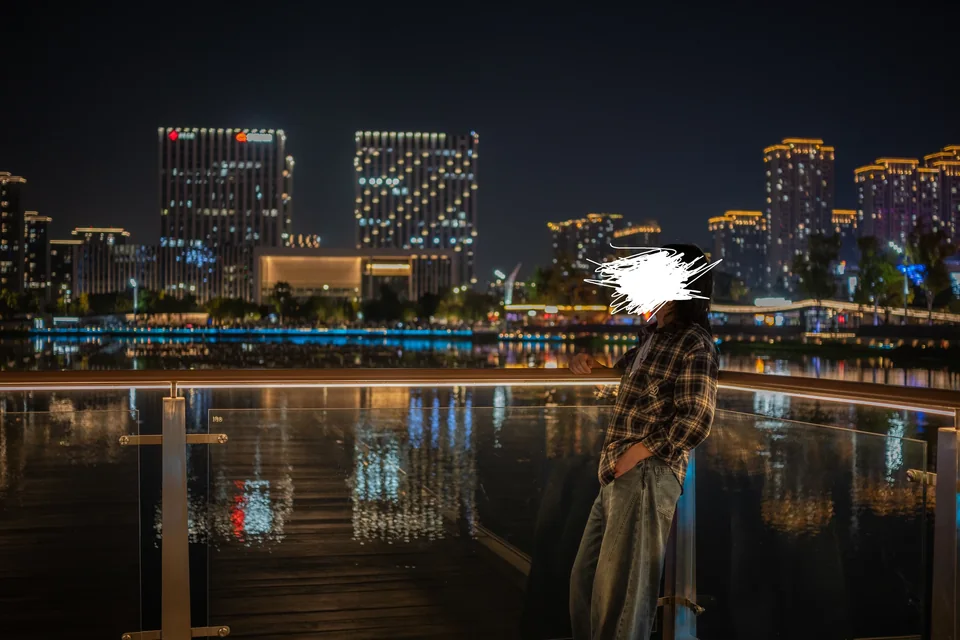 站在夜晚水边平台上的人，远处建筑灯光映在水中